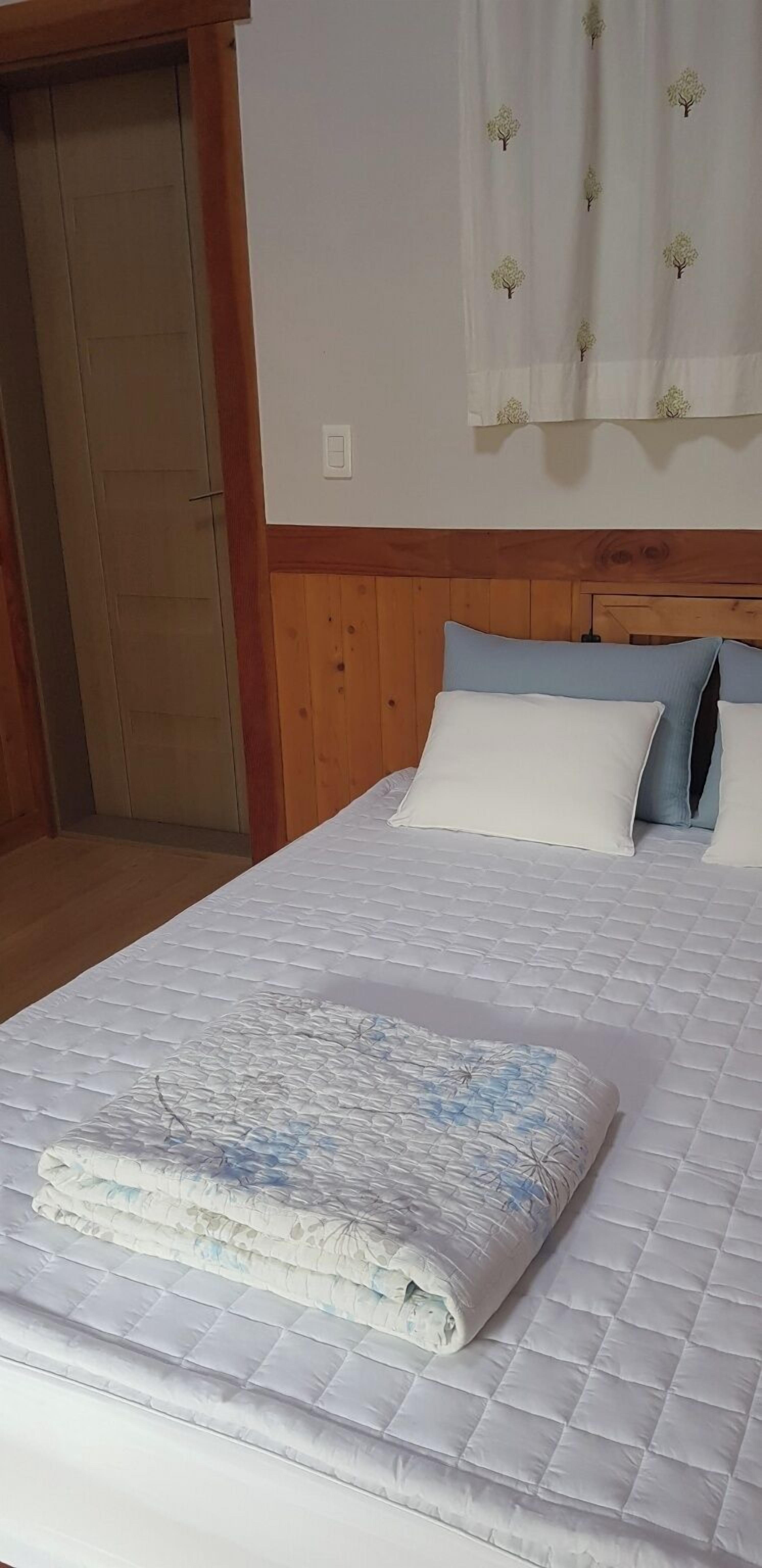 A bedroom with a wooden headboard, a bed with white and blue bedding, and a window with a floral curtain.