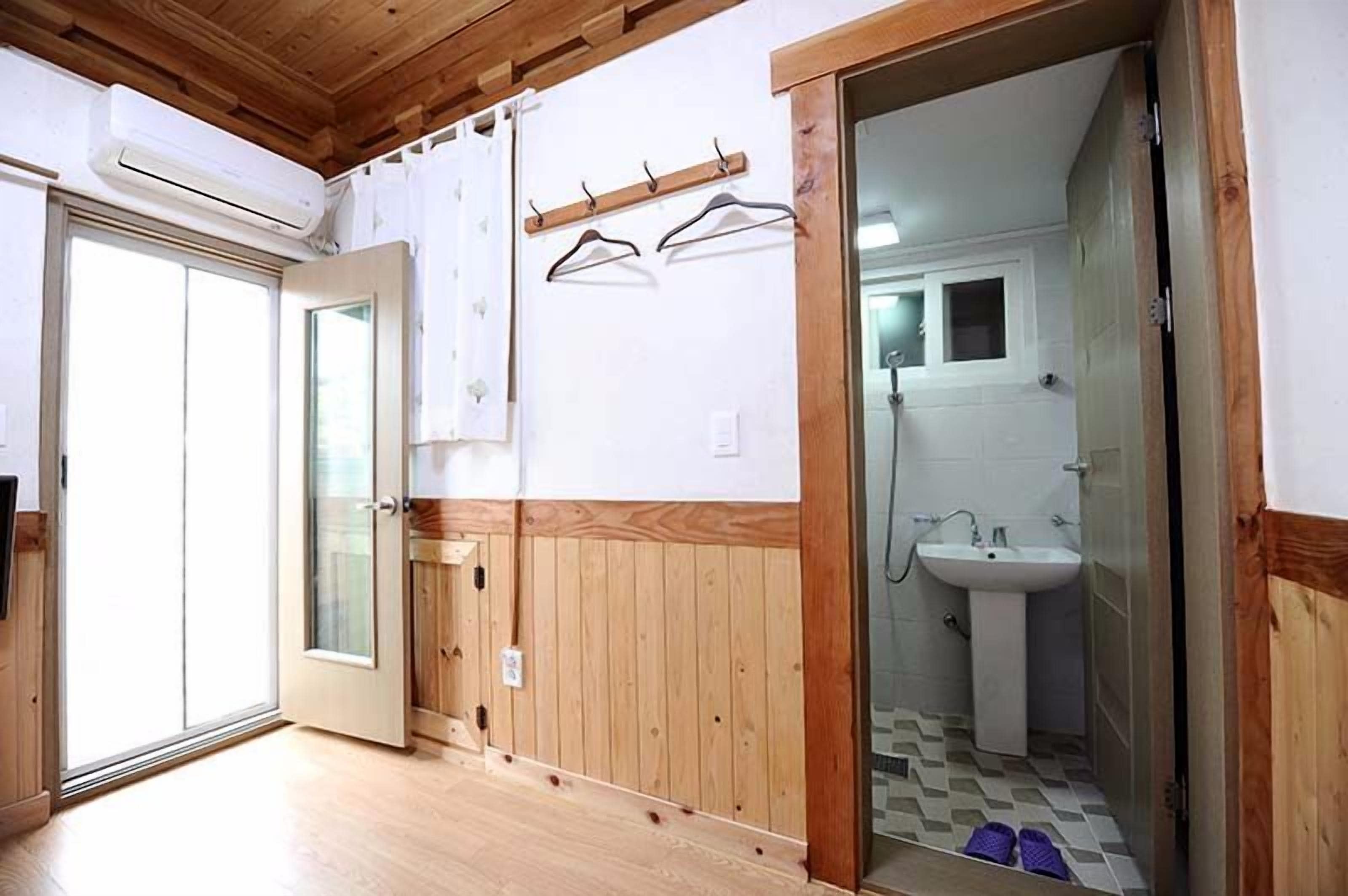 A room with a wooden floor, a sliding glass door, a white sink, and a wooden door.