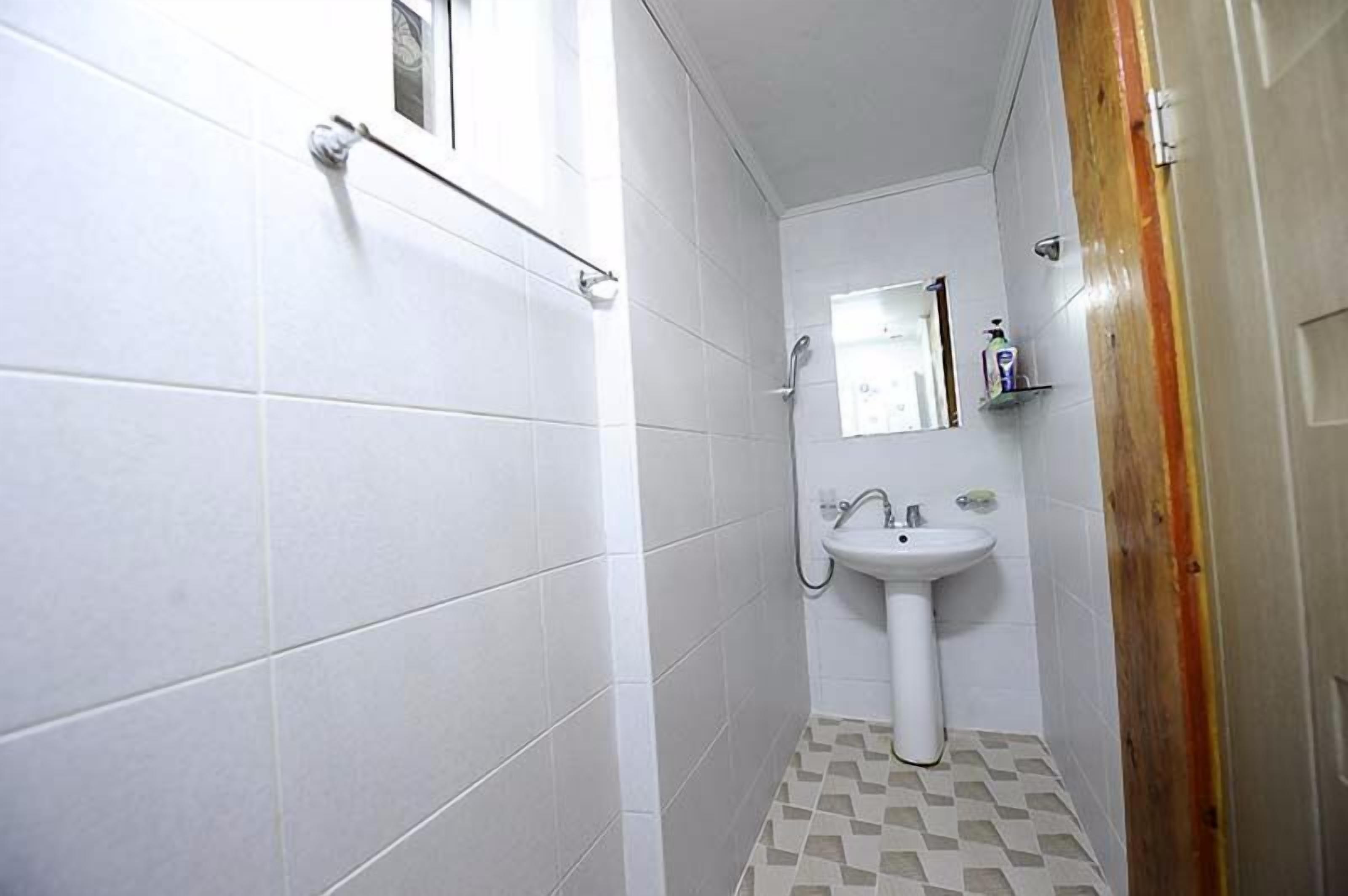 A small bathroom with white tiles, a sink, a mirror, and a shower.
