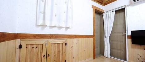 A room with wooden walls and ceiling, a sliding glass door, a white curtain, and a flat-screen TV mounted on the wall.