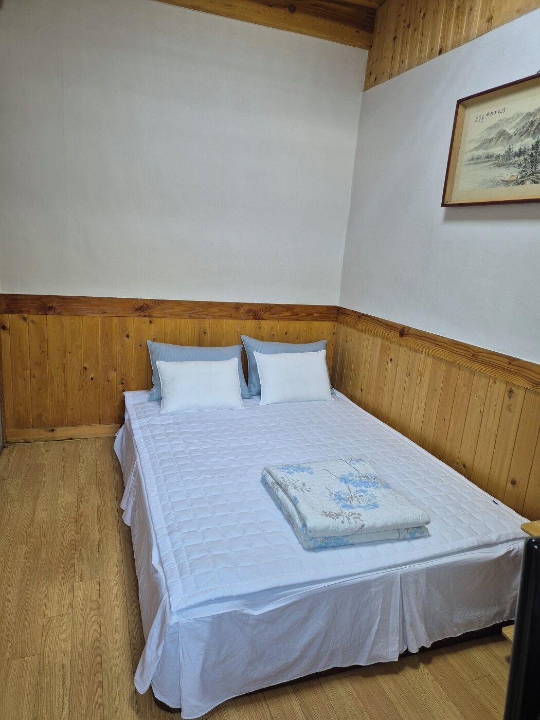 A single-bed room with a wooden headboard, white bedding, and a framed picture on the wall.