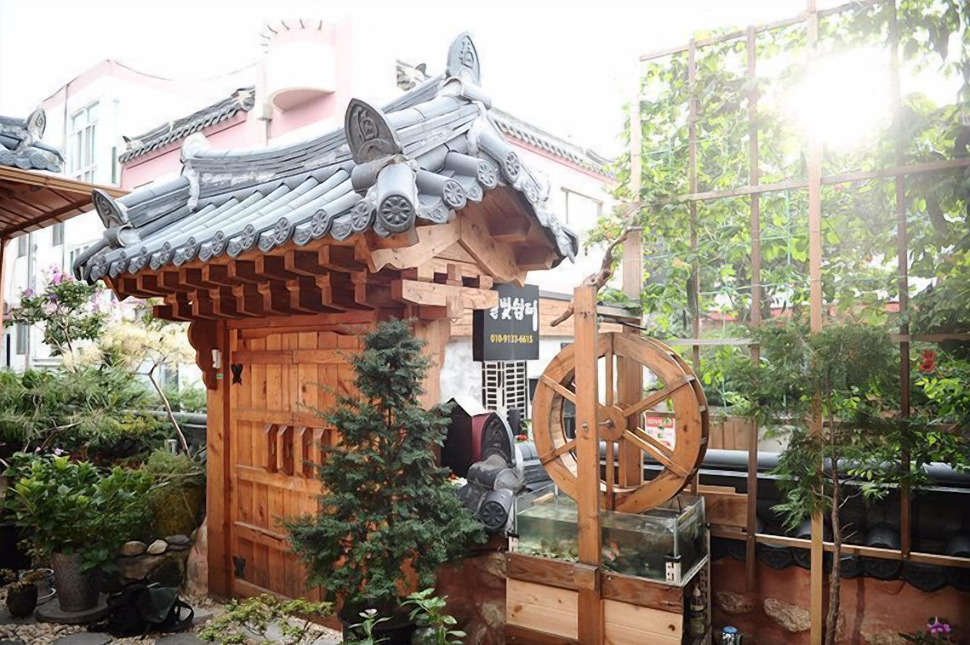 A traditional Japanese-style building with a wooden gate, a large wooden wheel, and a sign with contact information.