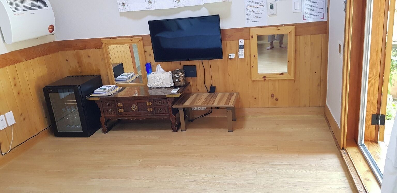 A room with a wooden floor, a TV mounted on the wall, a small wooden cabinet, and a bench.