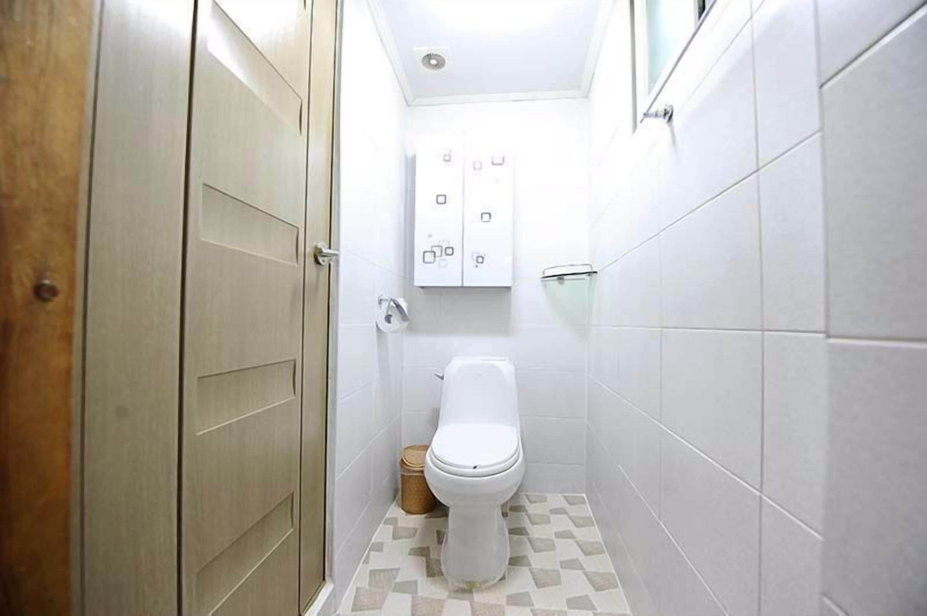 Un baño pequeño y estrecho con un inodoro, un cesto de basura y un panel eléctrico en la pared.