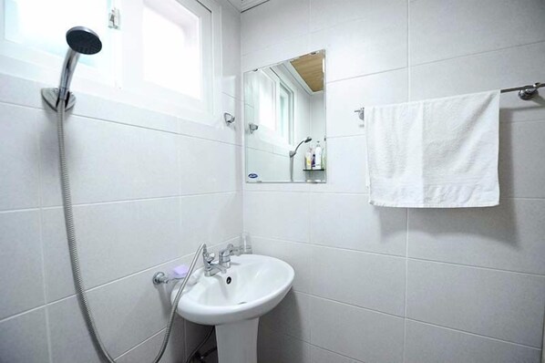 Baño con azulejos blancos, lavamanos, ducha de mano, toallero y espejo.