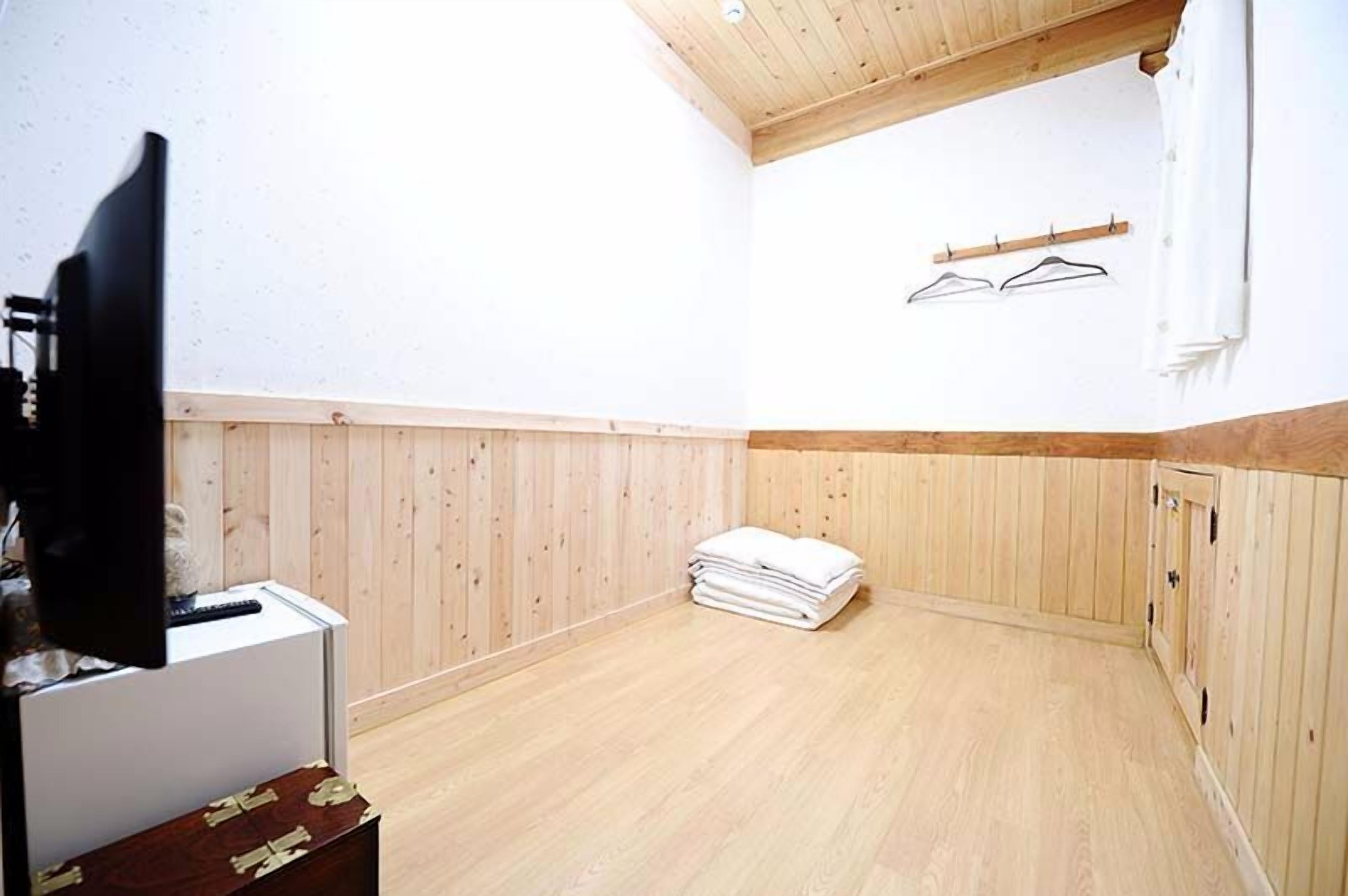 Una habitación con paredes y techo de madera, un televisor de pantalla plana sobre un soporte, una pila de toallas blancas y un mueble de madera.