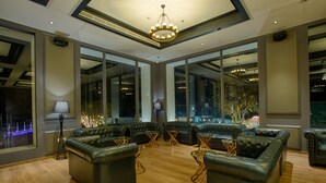 A spacious lounge area with leather sofas and tables, large windows offering views of the outside, and a modern chandelier. - The Four Vedas Hotel & Resort (Siliguri)