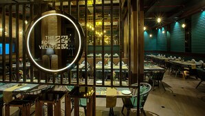 A restaurant with a modern interior, featuring a circular mirror with text, wooden beams, and a variety of dining tables and chairs. - The Four Vedas Hotel & Resort (Siliguri)