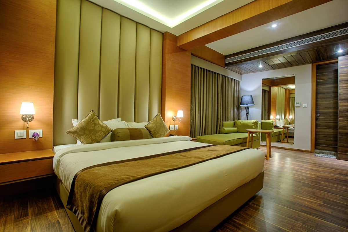 A hotel room with a large bed, a green sofa, a small table, and a mirror.