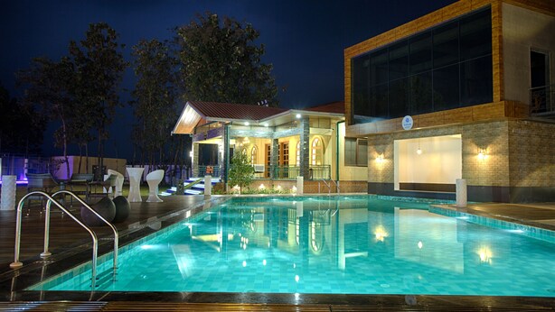 A swimming pool with a modern building in the background, a covered seating area, and a well-lit environment. - The Four Vedas Hotel & Resort (Siliguri)