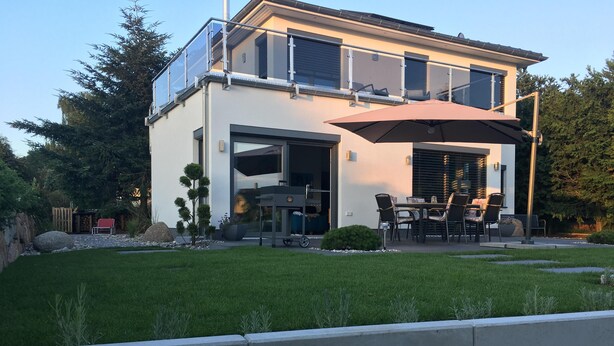 A modern two-story house with a patio area featuring outdoor furniture and a large umbrella.