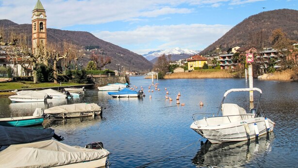 A calm lake with boats docked, a clock tower, and mountains in the background. - Lungolago by Interhome (Lavena Ponte Tresa)