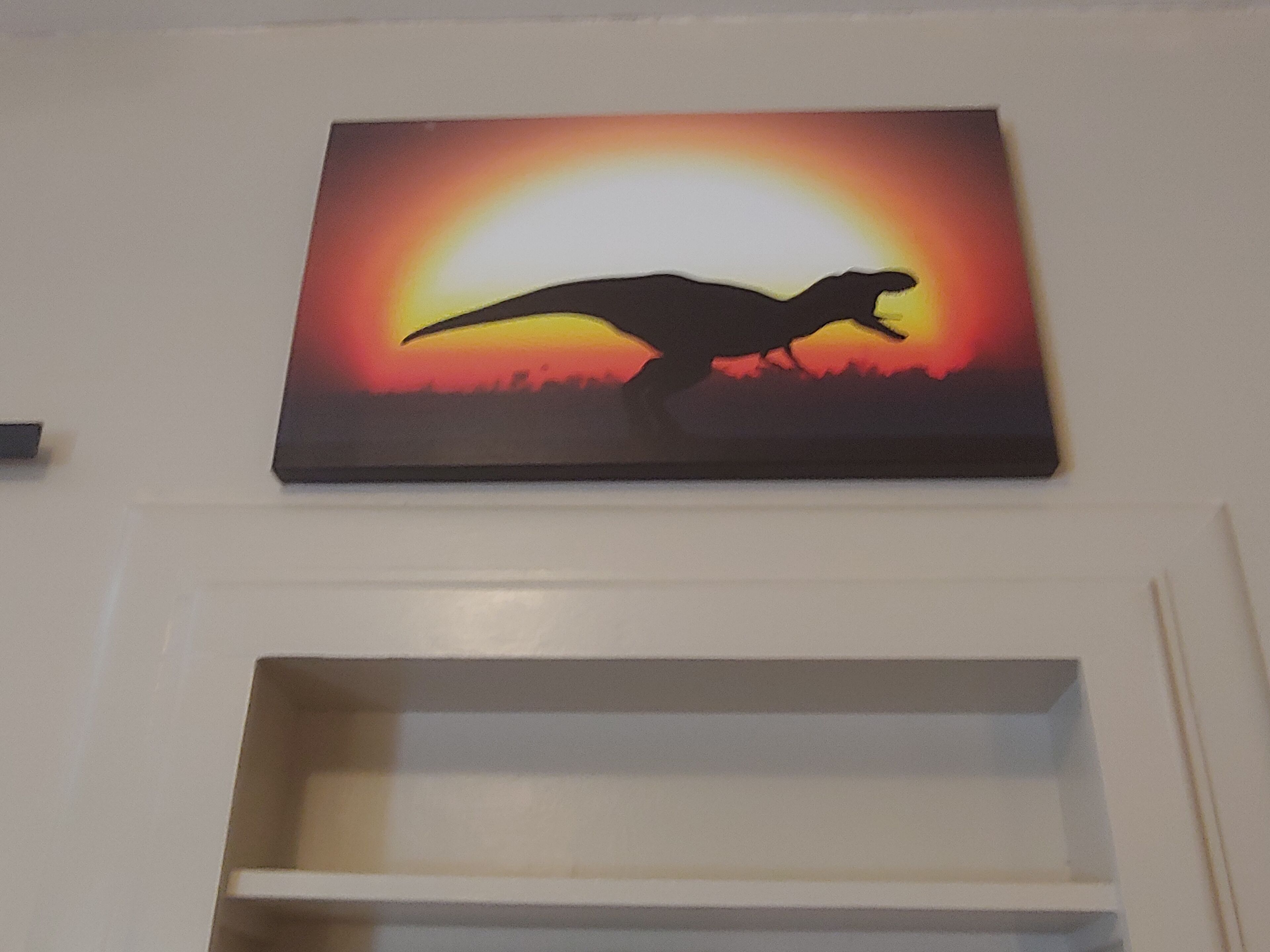 En vägg med en målning som föreställer en dinosauriesiluett mot en solnedgång.