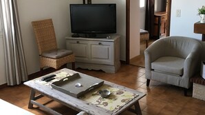 A living room with a television on a cabinet, a chair, a table with a tray, and a bed. - First floor single house (Querciolo)