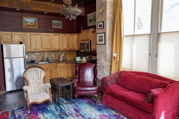 La cuisine est équipée de meubles en bois, d’un réfrigérateur et d’un four à micro-ondes. Le salon comprend un fauteuil en cuir rouge et un canapé rouge.