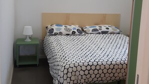 Pieni, siististi järjestetty makuuhuone, jossa on sänky, yöpöytä lampun kanssa ja vihreä yöpöytä.