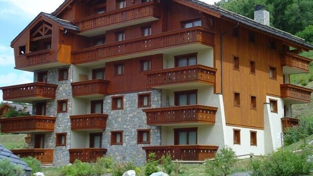 Un immeuble en bois à plusieurs étages, doté de balcons et agrémenté de détails en pierre, avec une chaîne de montagnes en arrière-plan.