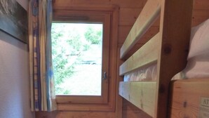 Une cabine avec une petite fenêtre, des lits superposés en bois et une armoire en bois avec des tiroirs.