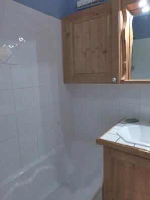 A bathroom with a bathtub, a wooden cabinet, and a mirror. - 150m from shops, 1st floor, balcony, tv, 32m², Méribel (Méribel - Les Allues)