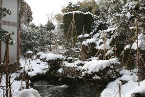 Ein traditioneller japanischer Garten mit Teich für Koi-Karpfen, schneebedeckten Bäumen und Holzbauten.