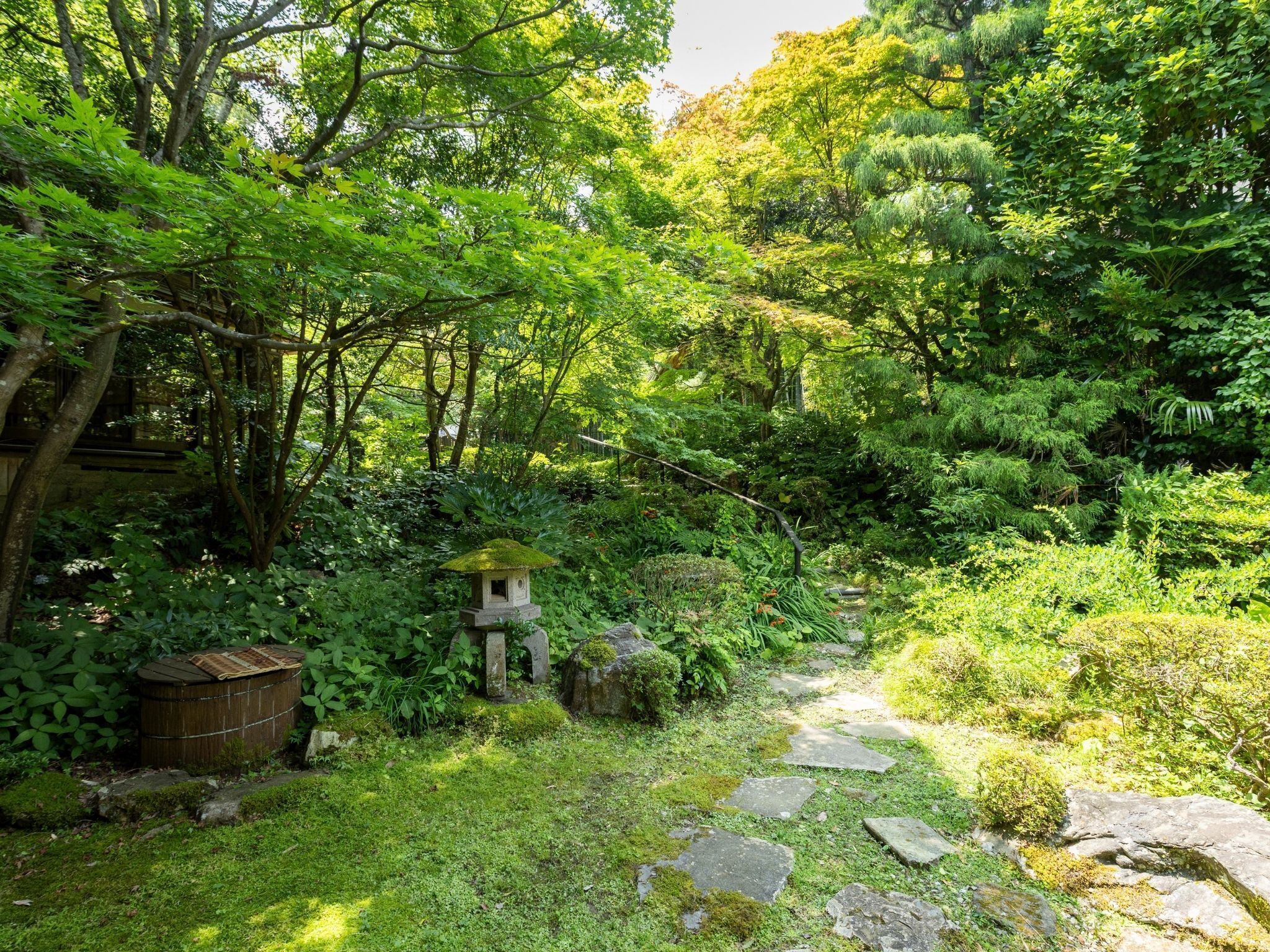 A lush garden with a stone path, moss-covered rocks, and a small stone structure.