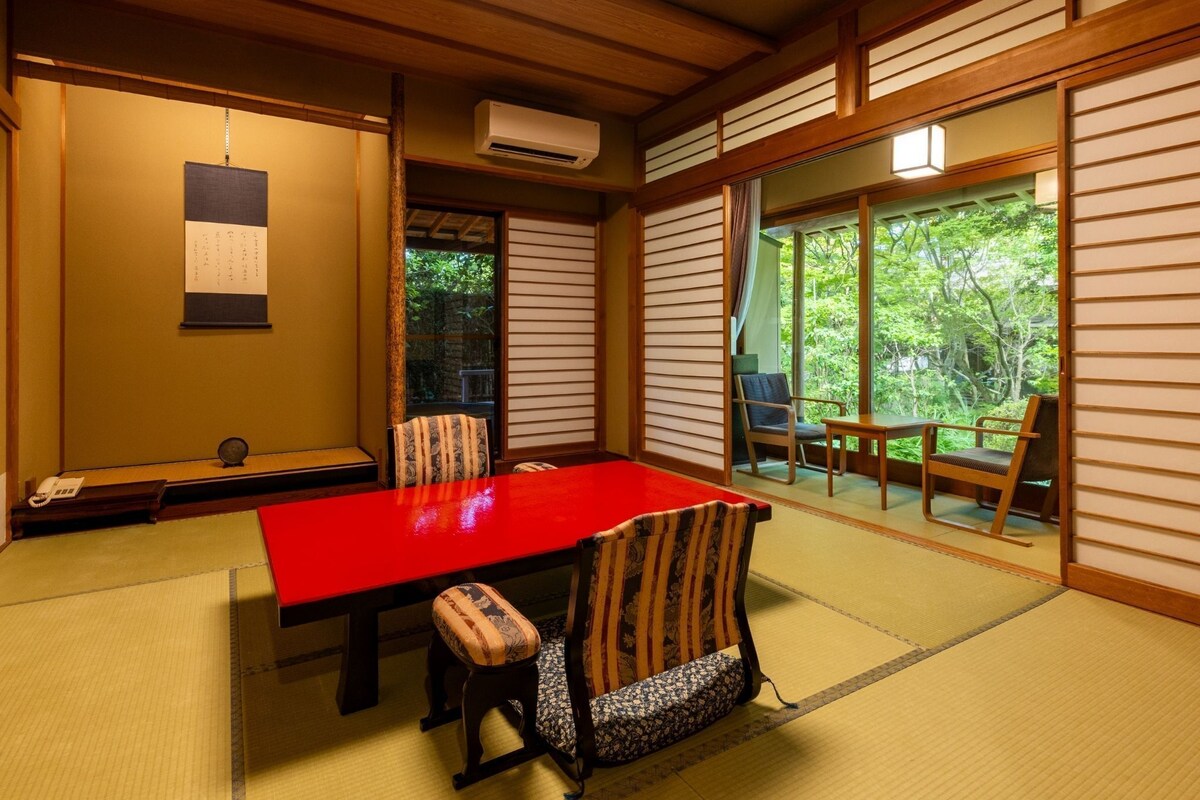 Ein traditioneller japanischer Raum mit Tatami-Boden, einem roten Tisch und verschiebbaren Shoji-Türen, die zu einem Garten führen.