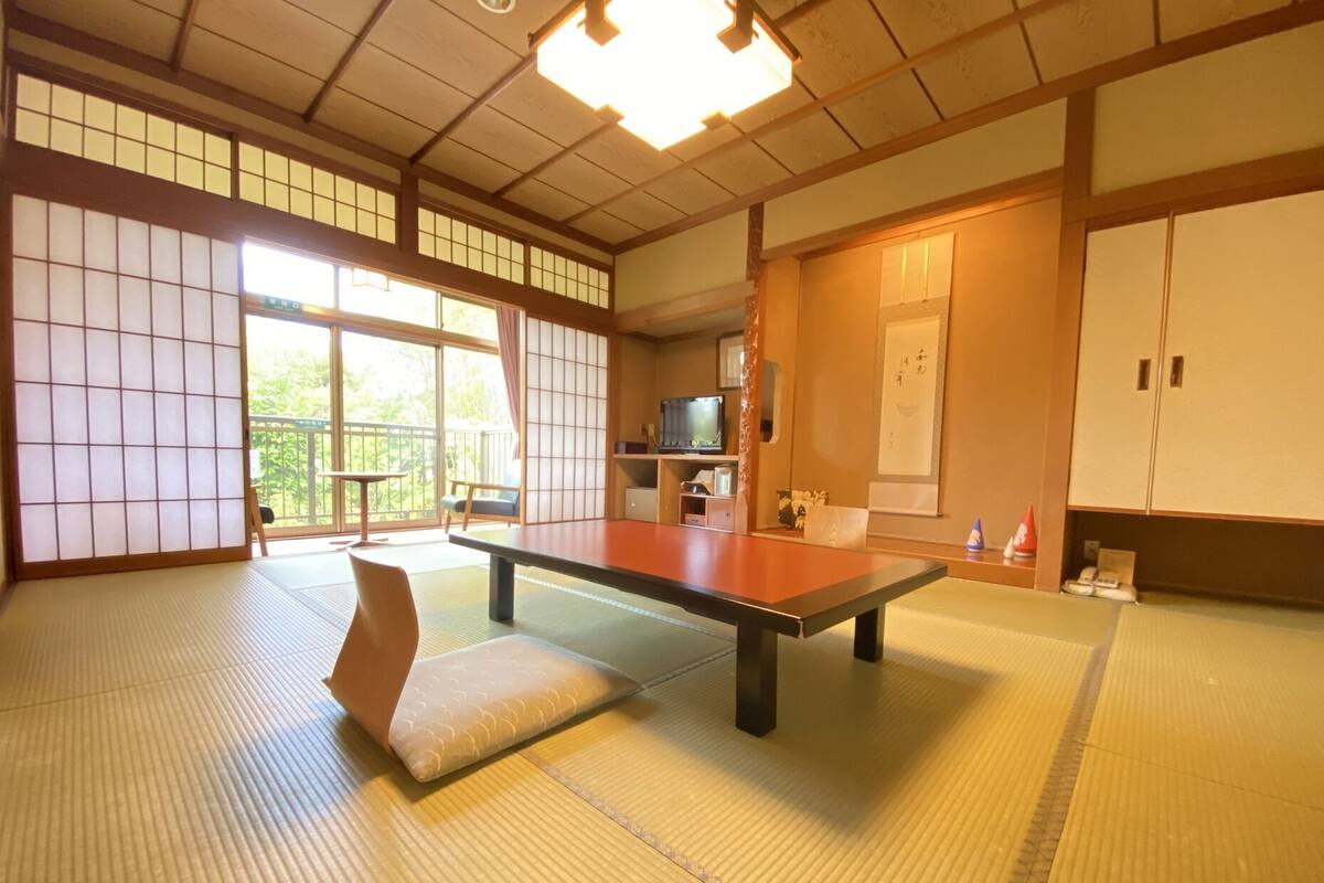 A tatami mat room with a low table, cushions, sliding doors, and a television.