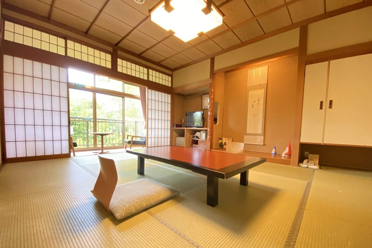 A tatami mat room with a low table, cushions, sliding doors, and a television.