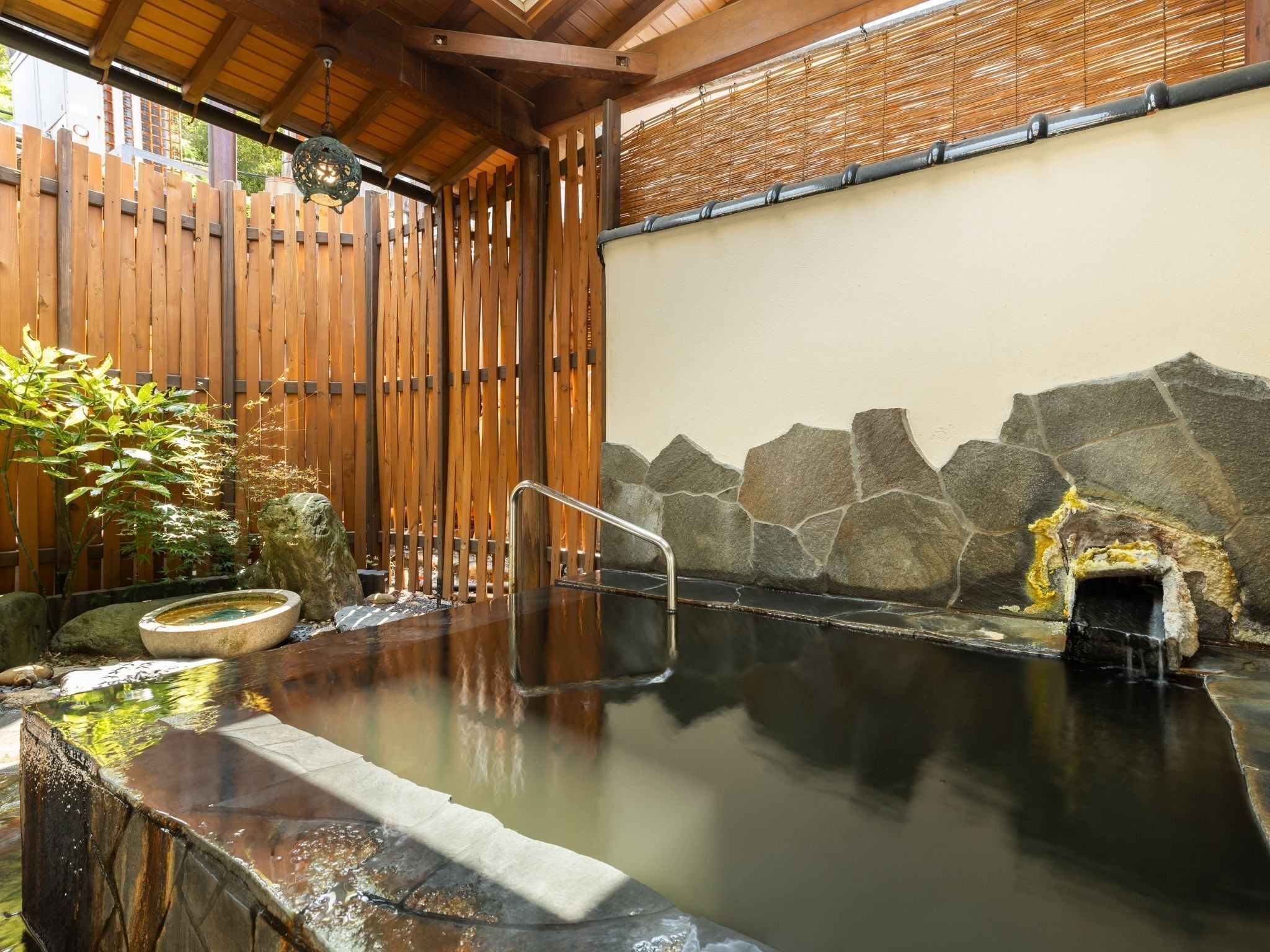 A traditional hot spring bath area with a wooden fence, stone wall, and a stone basin.