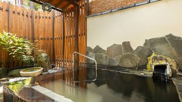 A traditional hot spring bath area with a wooden fence, stone wall, and a stone basin.