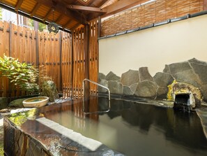 A traditional hot spring bath area with a wooden fence, stone wall, and a stone basin.