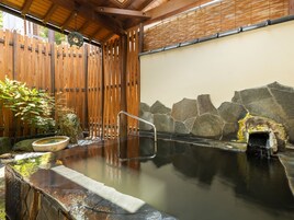 A traditional hot spring bath area with a wooden fence, stone wall, and a stone basin.