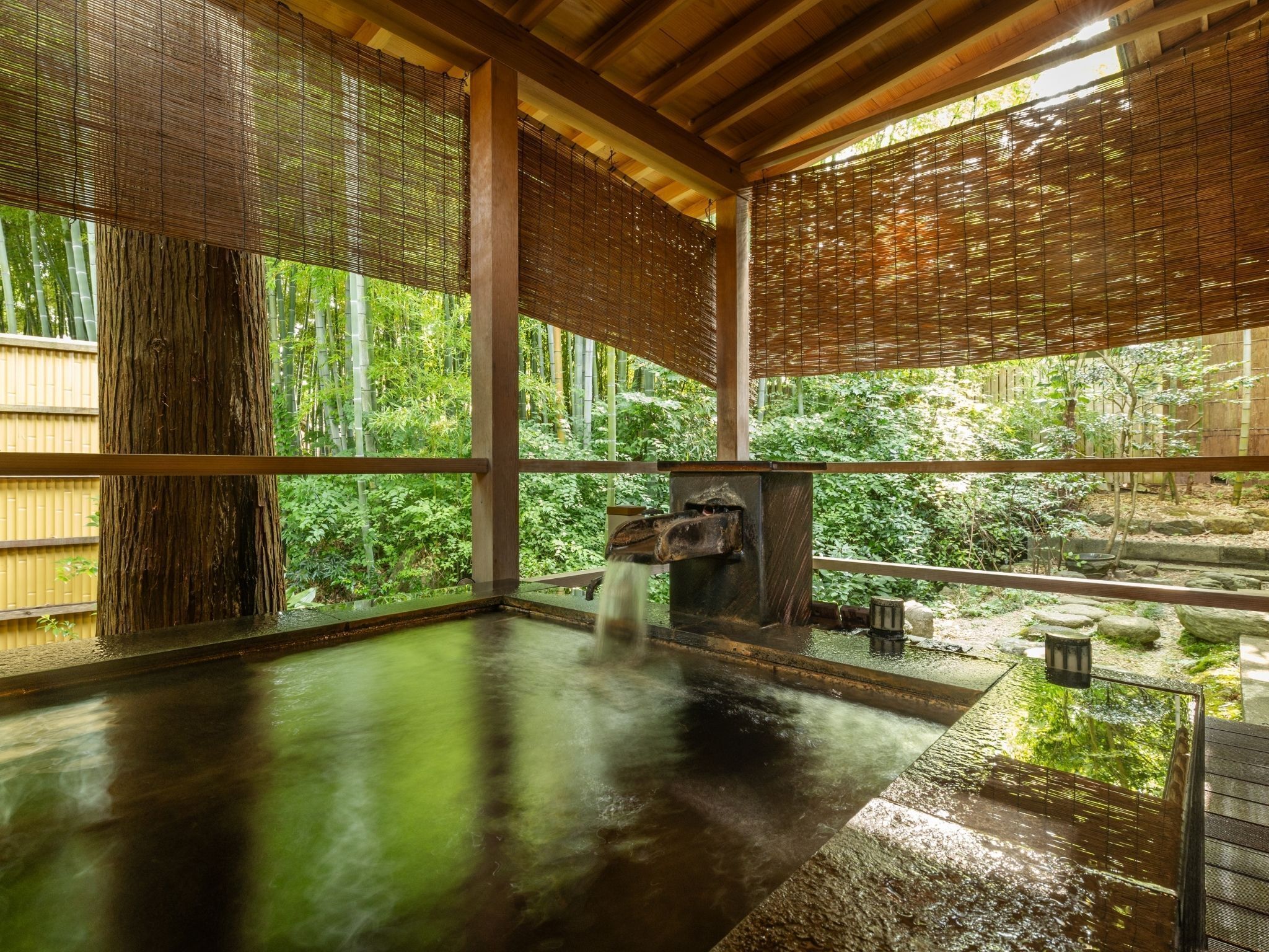 Un onsen japonés tradicional con interior de madera, una batea de piedra y vistas a exuberante follaje.