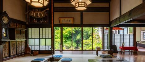 A traditional Japanese room with tatami flooring, a shoji screen, and a view of greenery outside.