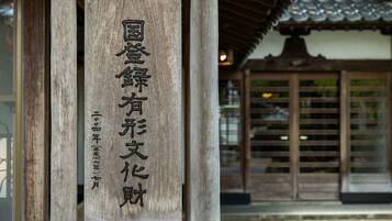 Ein hölzernes Schild mit japanischen Schriftzeichen, Teil eines traditionellen Gebäudes mit einem Ziegeldach und Holztüren.