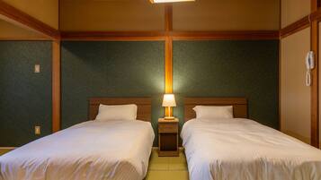 A hotel room with two beds, a nightstand with a lamp, wooden paneling, and a telephone.