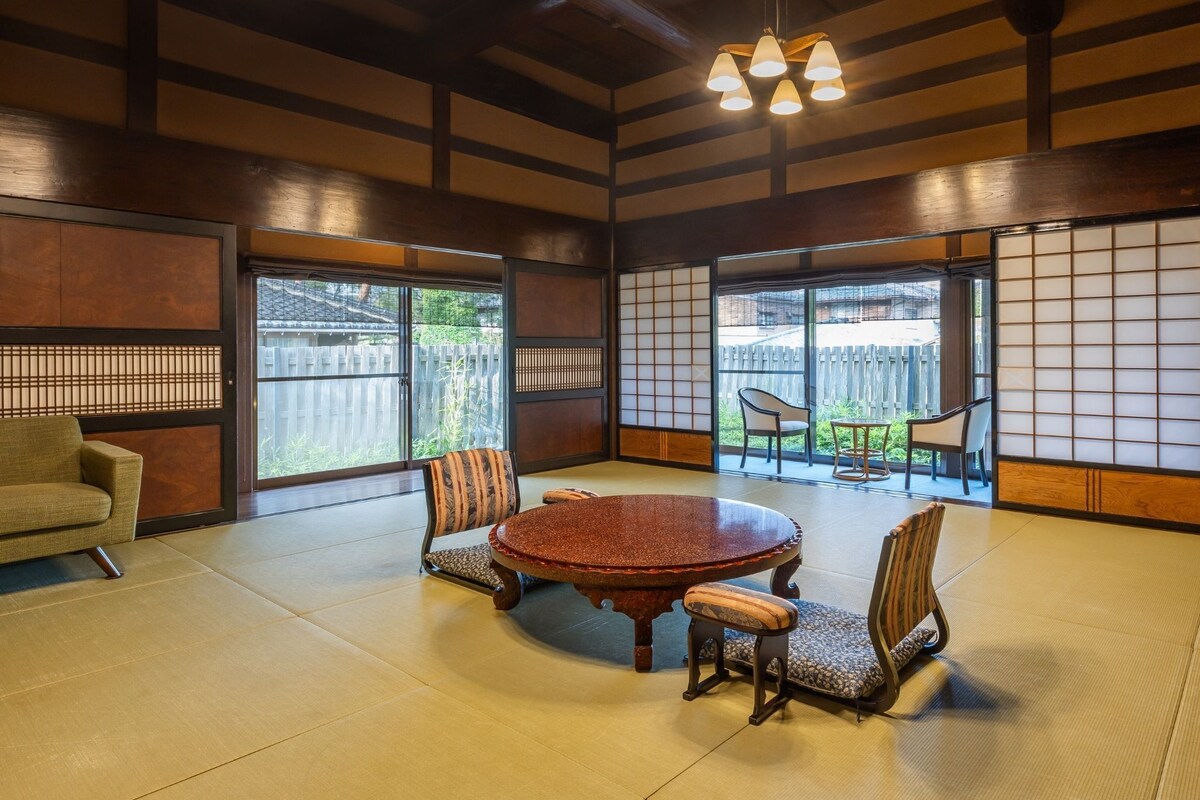 Ein traditioneller japanischer Raum mit Tatami-Böden, einem runden Tisch und niedrigen Holzstühlen.