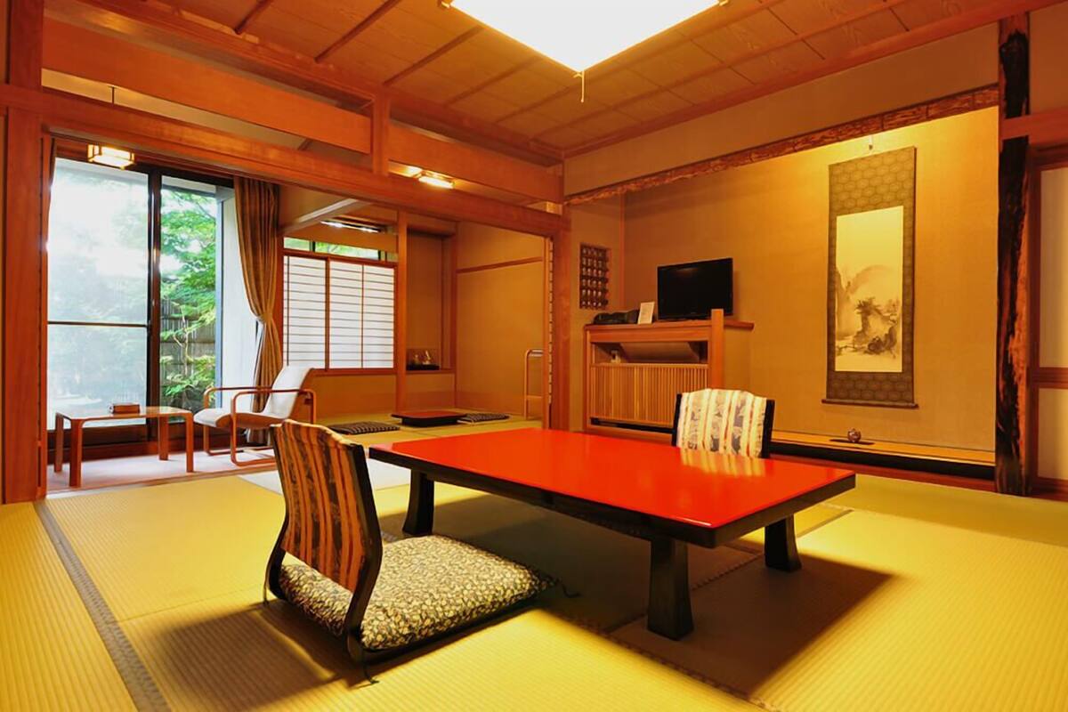 A traditional Japanese room with tatami flooring, a low table, and a television on a shelf.