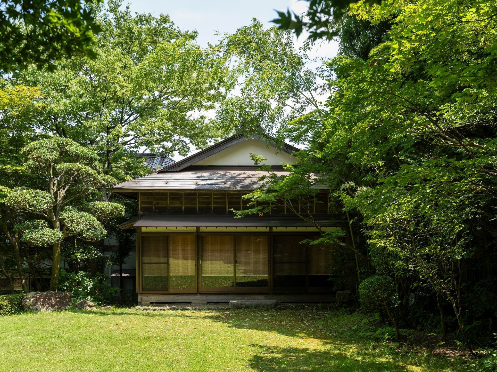 Une maison traditionnelle japonaise, dotée d’un toit en pente, entourée d’une végétation luxuriante et d’une pelouse bien entretenue.