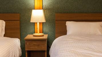A hotel room with two beds, a nightstand with a lamp, and a green textured wall.