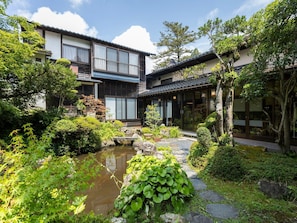 Een traditioneel Japans gebouw met een vijver met koi karpers en weelderig groen.