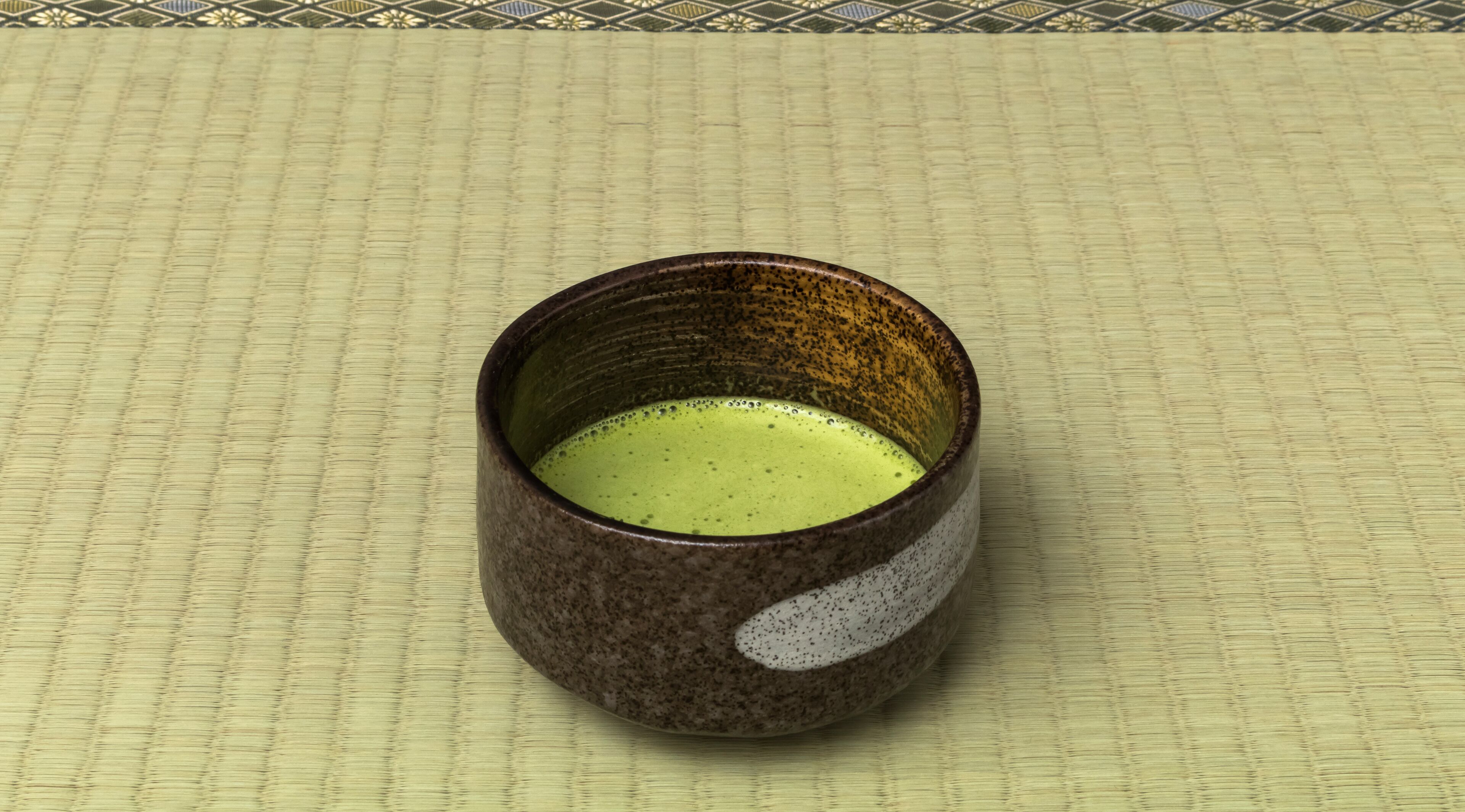 A ceramic mug with a speckled exterior and a white interior, placed on a woven mat.