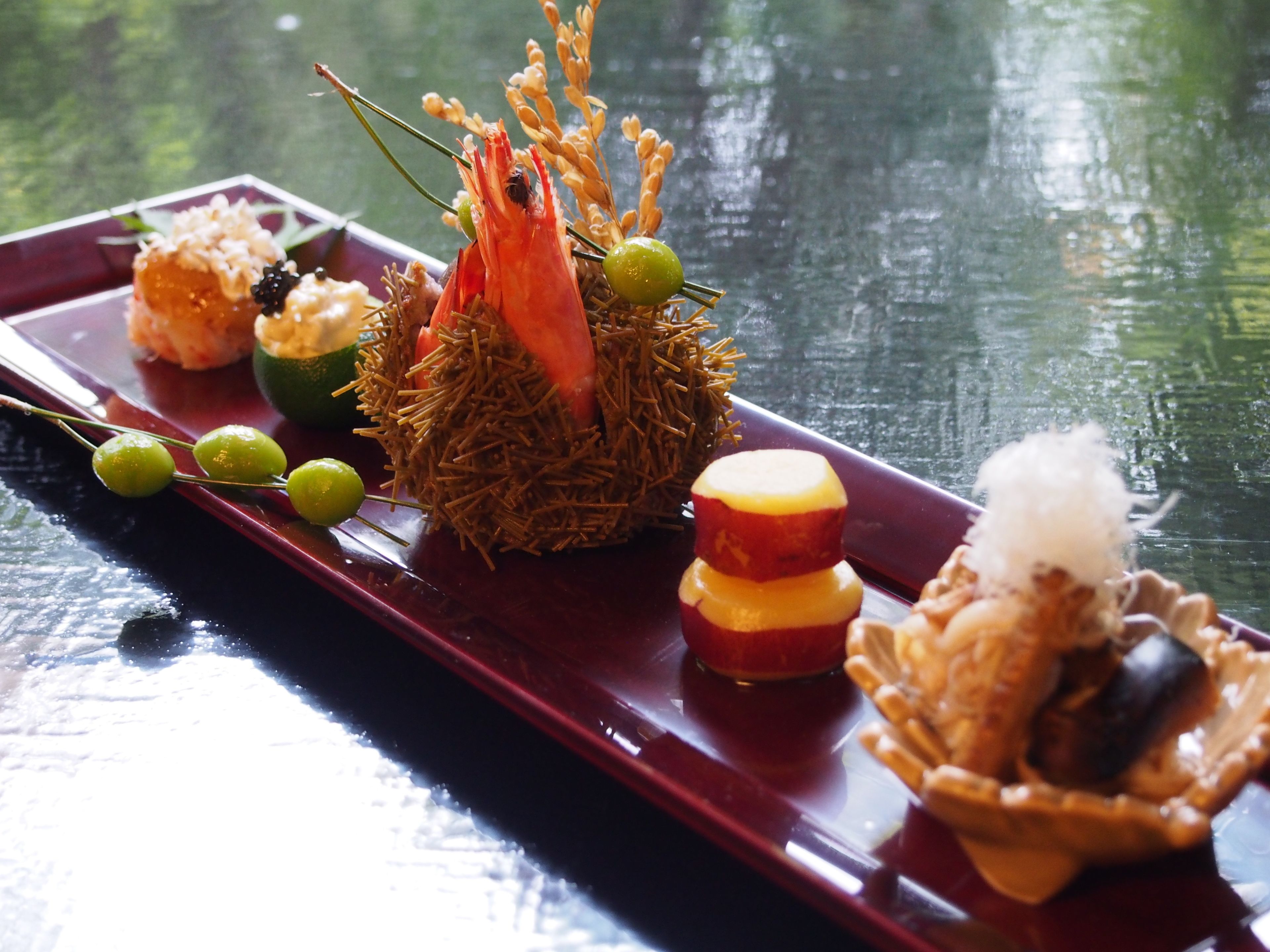A variety of dishes on a tray, including a central decorative item with a bird and greenery, surrounded by smaller food items.