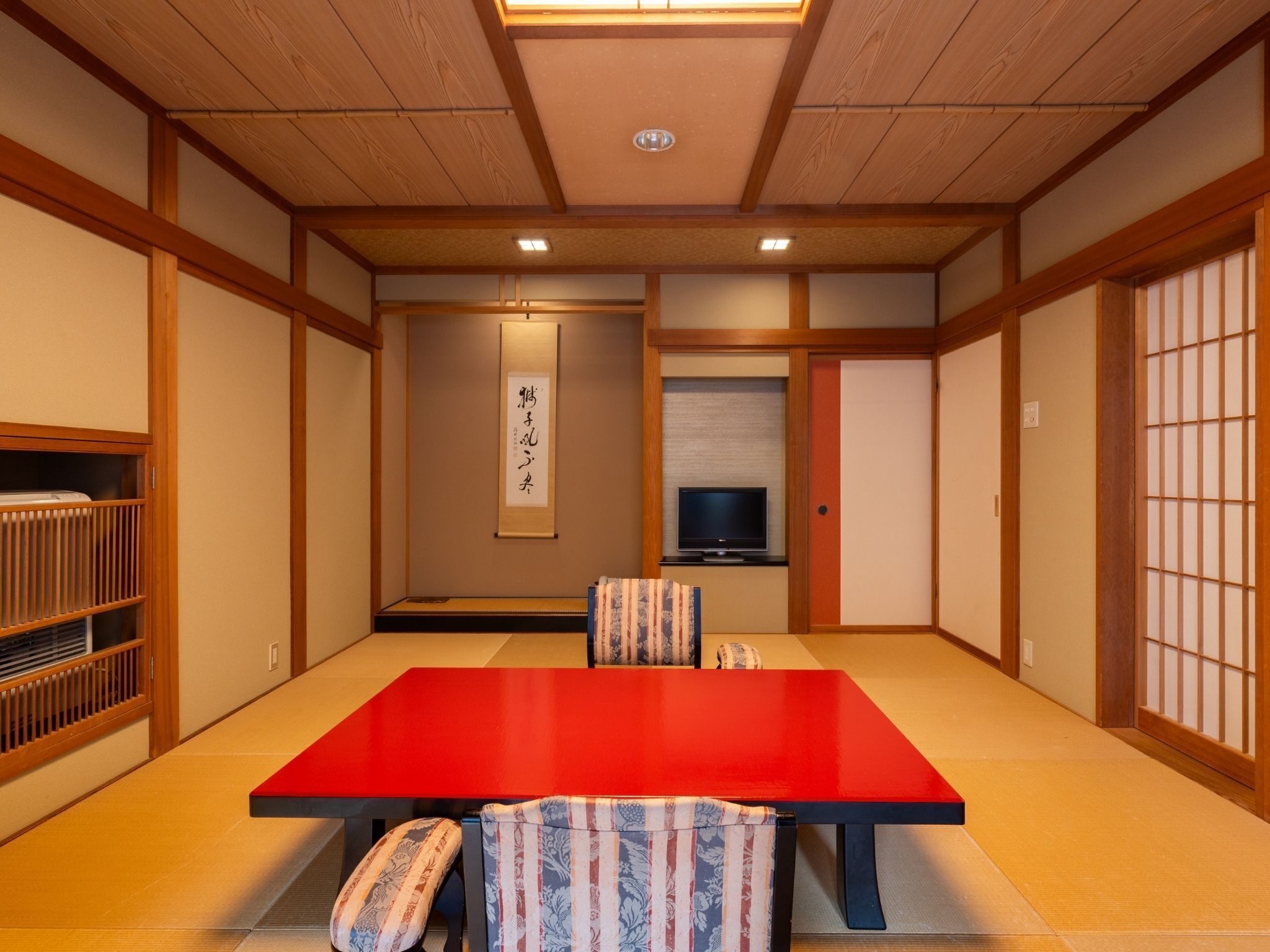 Ein traditioneller japanischer Raum mit Tatami-Bodenbelag, einem roten Tisch und Schiebetüren.