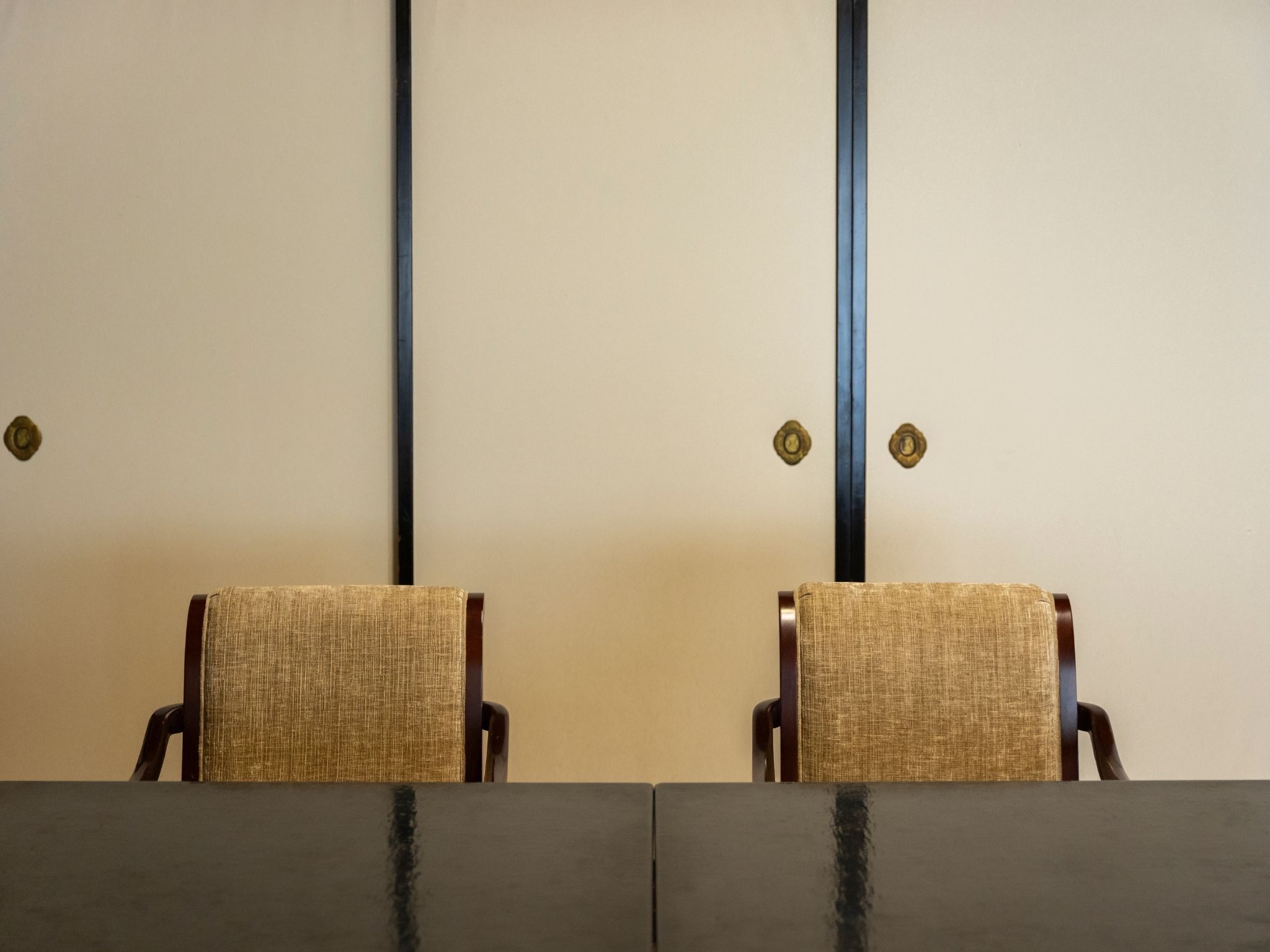 Two chairs with woven fabric backs and dark wooden frames, positioned at a table with a dark surface.