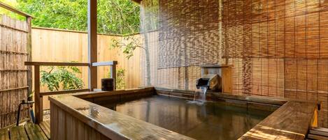A hot spring bath area with a wooden deck, bamboo wall, and a wooden bench.