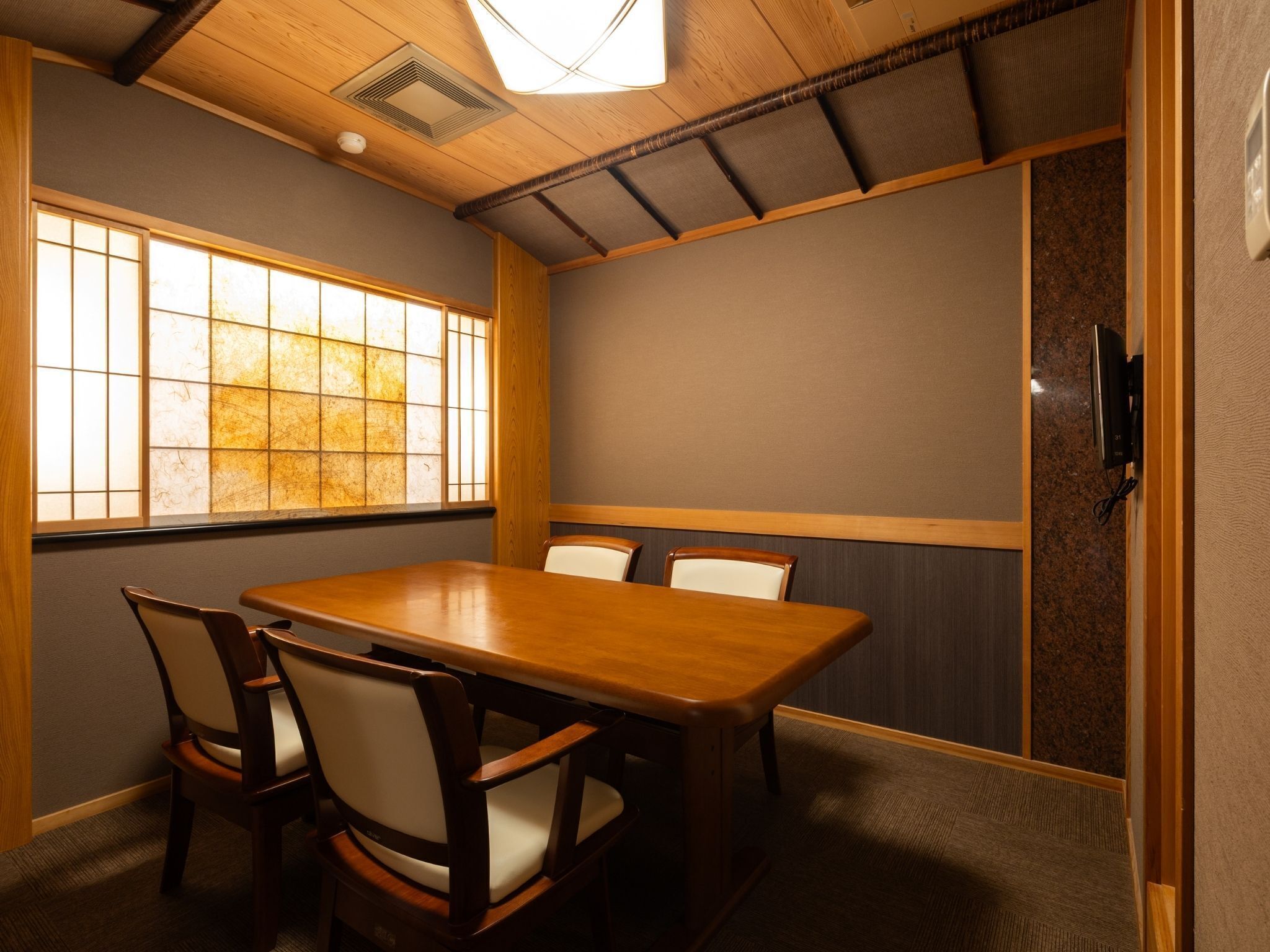 Een vergaderruimte met een houten tafel en stoelen, een groot raam en een traditionele Japanse schuifdeur.