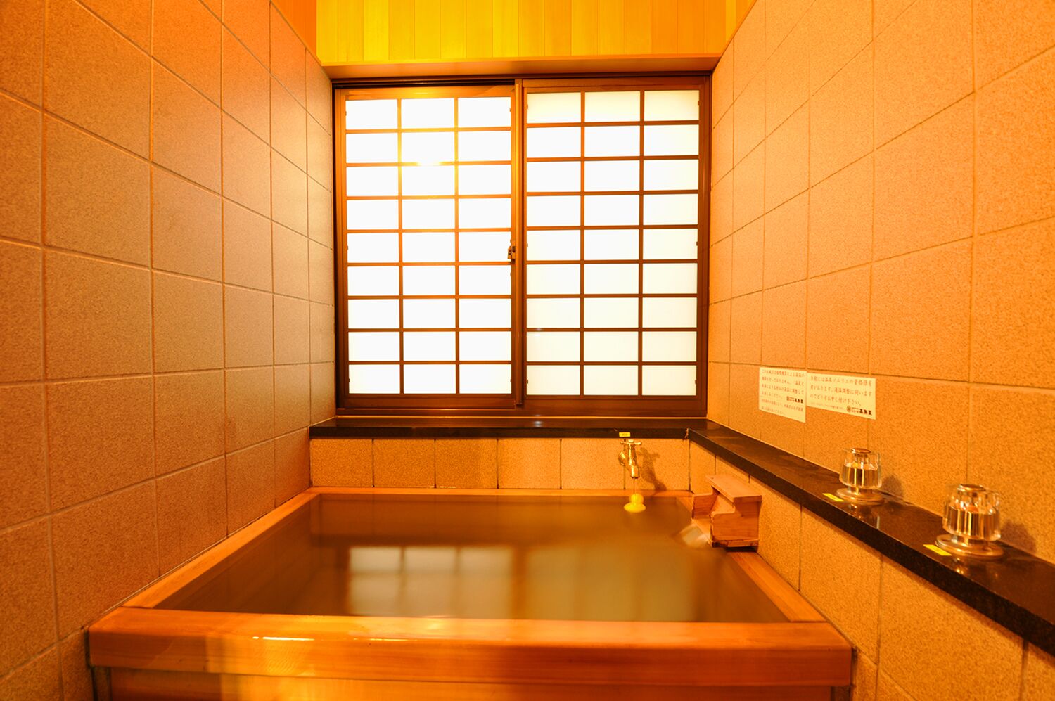 Um banheiro em estilo japonês tradicional, com uma banheira de madeira, janela com padrão quadriculado e paredes revestidas de azulejos.