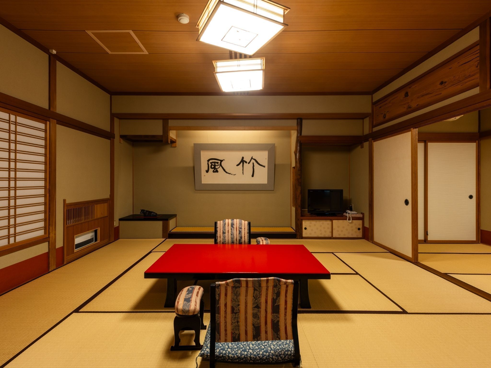 Una habitación tradicional japonesa con suelo de tatami, una mesa roja y un televisor.
