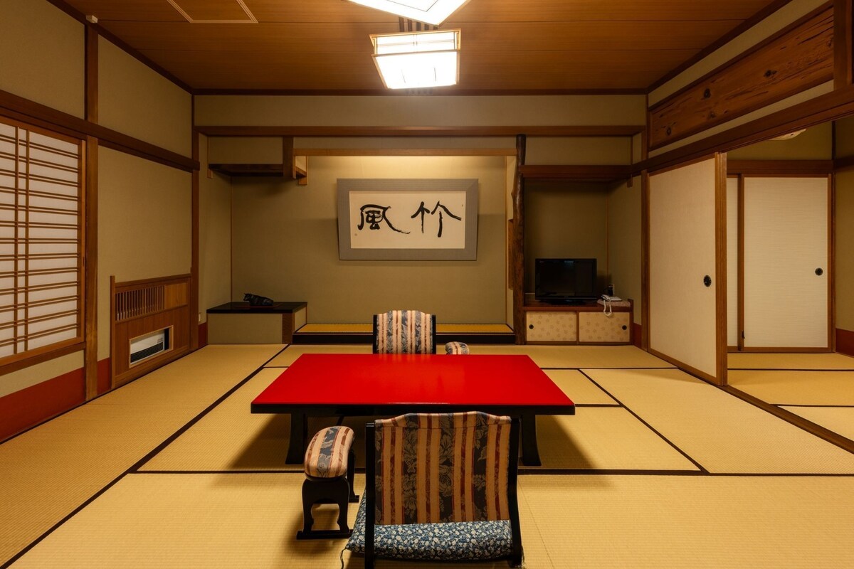Ein traditioneller japanischer Raum mit Tatami-Bodenbelag, einem roten Tisch und einem Fernseher.